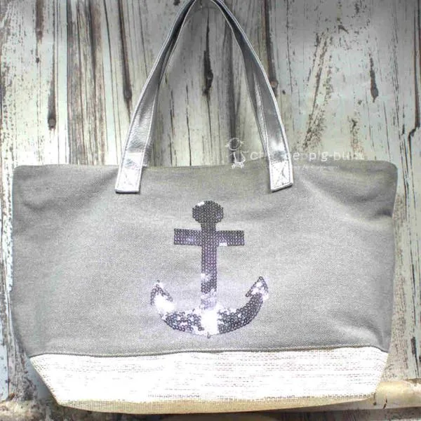 Graue Shoppertasche mit silbernem Pailletten-Anker, weißem Boden mit Silberstreifen und grauen Kunstleder-Griffen vor rustikalem Holzhintergrund.